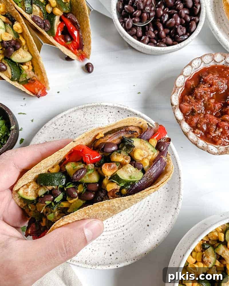Roasted Harvest Tacos 2 Vegan Roasted Veggie Tacos beautifully arranged on a white plate, with fresh ingredients like corn, zucchini, and peppers blurred in the background on a clean white surface.