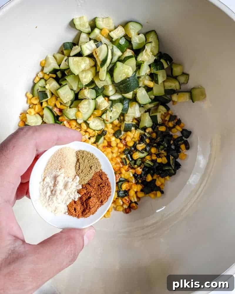 Roasted Harvest Tacos 11 spices being added to various roasted vegetables in a white bowl against a white background.