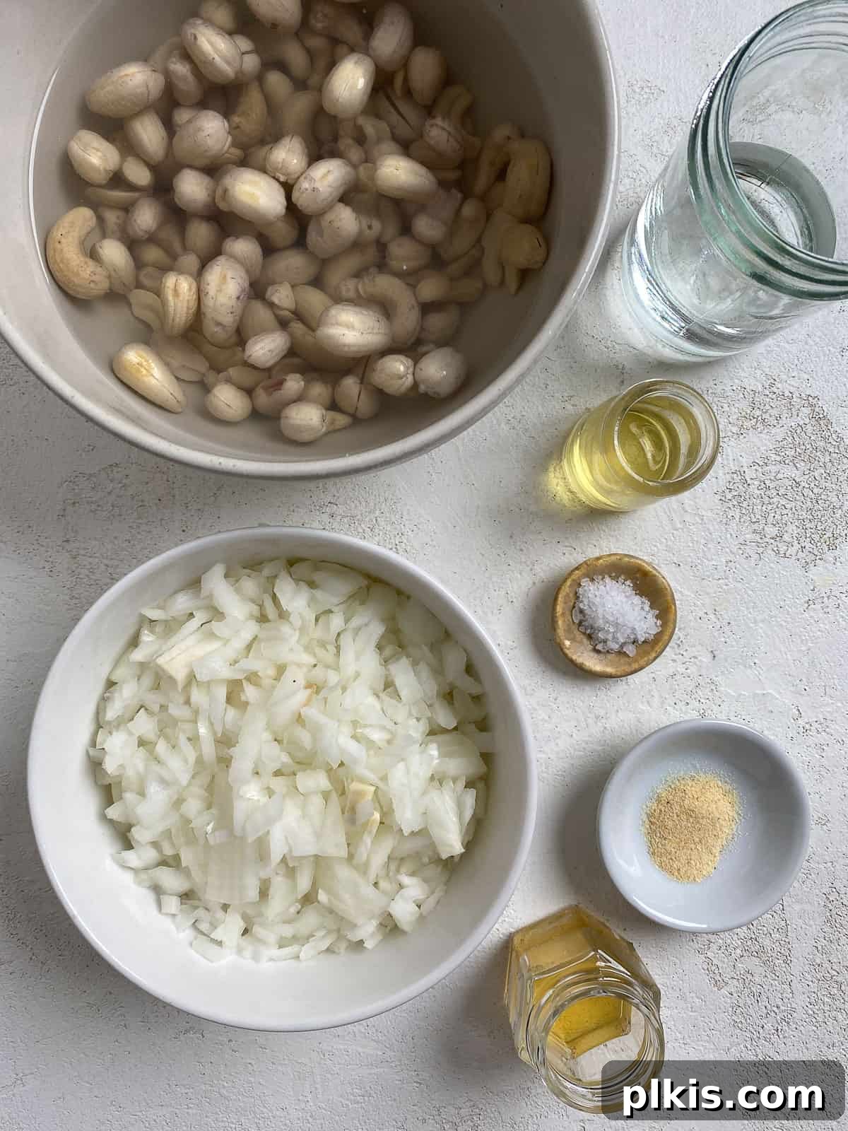 Gourmet Vegan French Onion Dip 3 A curated selection of fresh ingredients for Vegan French Onion Dip, including raw cashews, chopped yellow onion, garlic powder, apple cider vinegar, and oil, neatly arranged on a white surface.