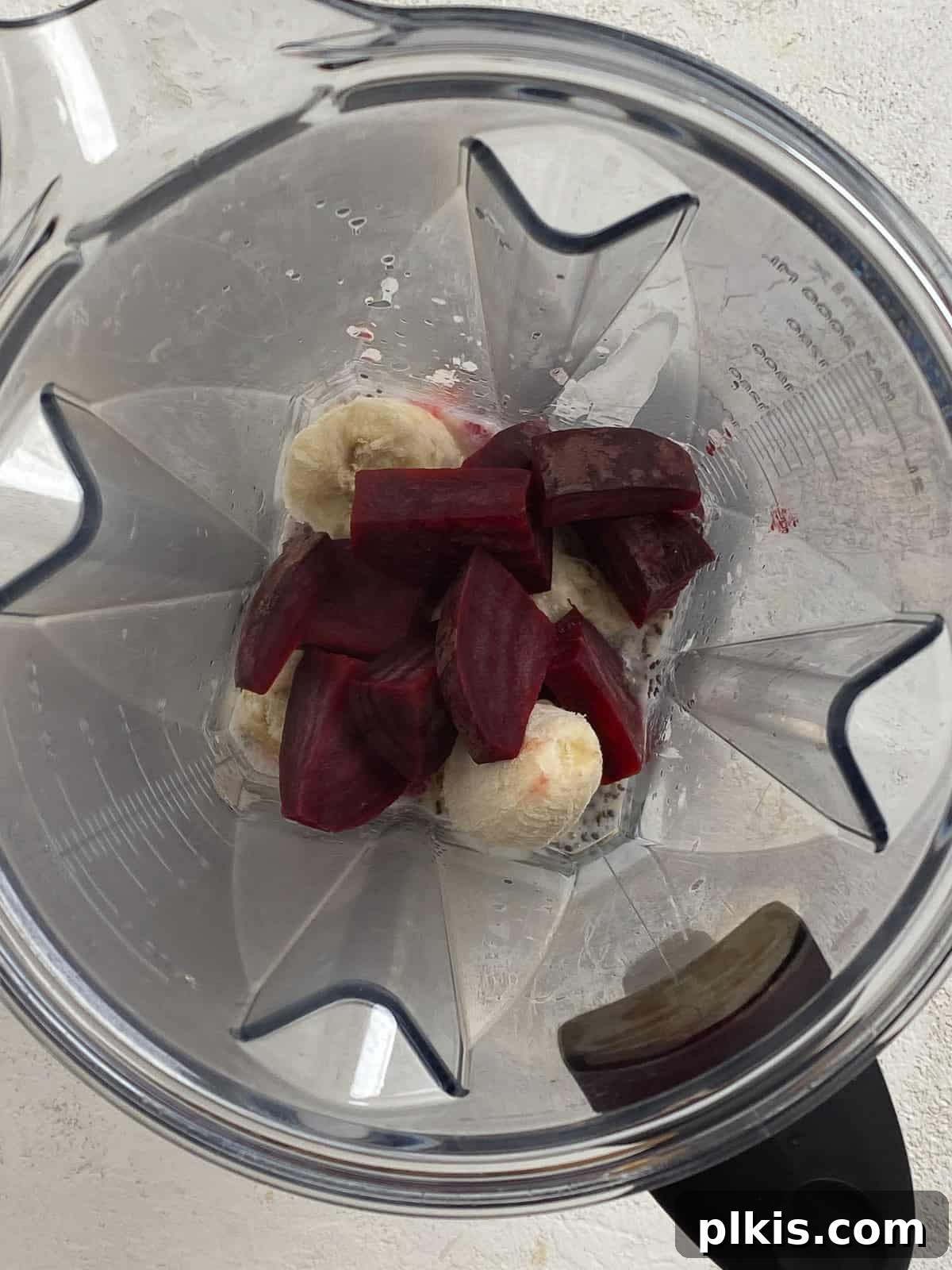 Ruby Red Beet & Banana Bliss 5 A clear glass blender jar filled with the pre-blended ingredients for the Banana Beet Smoothie, including banana, milk, lemon juice, and raspberries, ready for the beets.