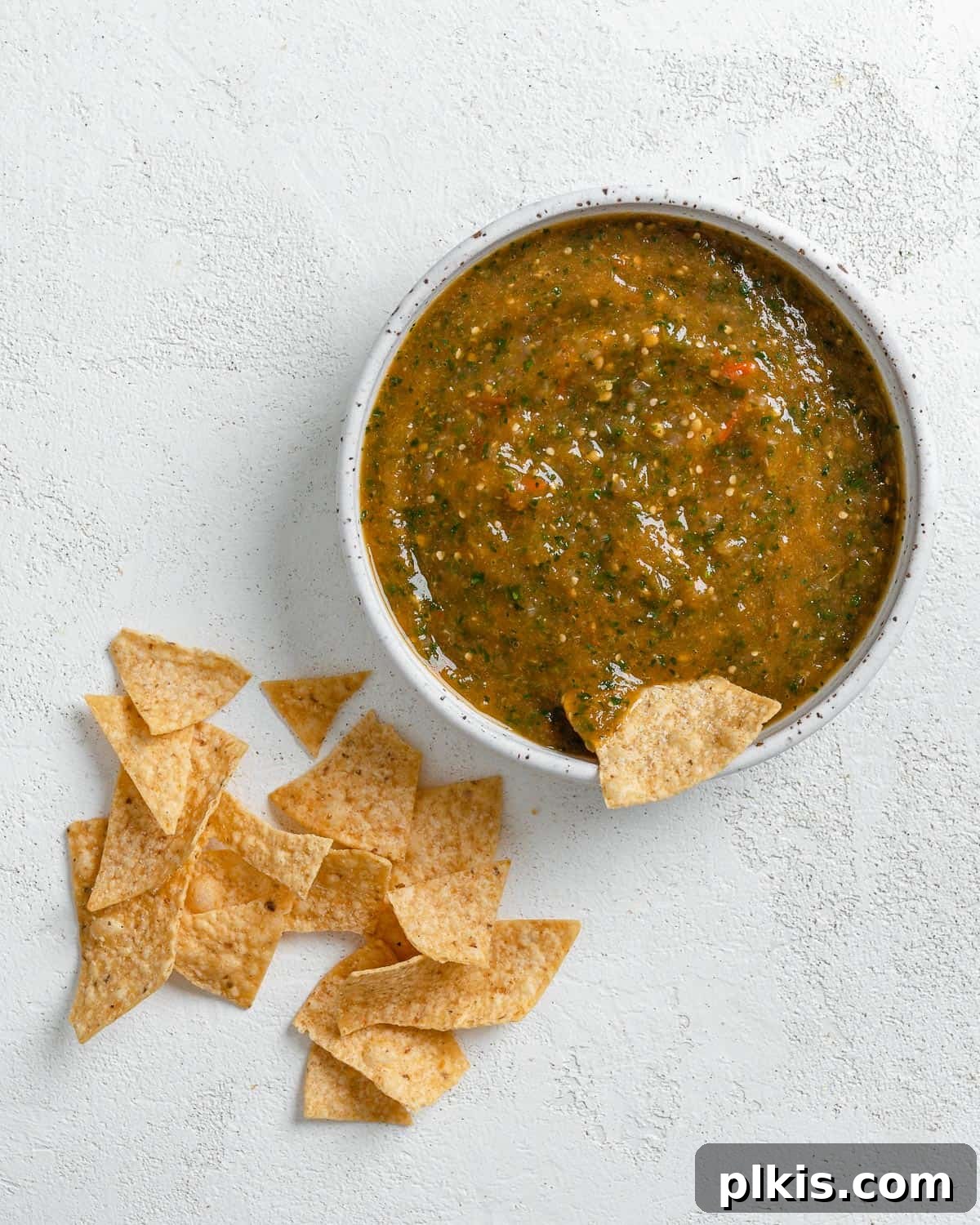 Zesty Tomatillo Green Chili Salsa 12 A bowl of freshly made stovetop tomatillo salsa with a chip being dipped in, surrounded by tortilla chips for serving.