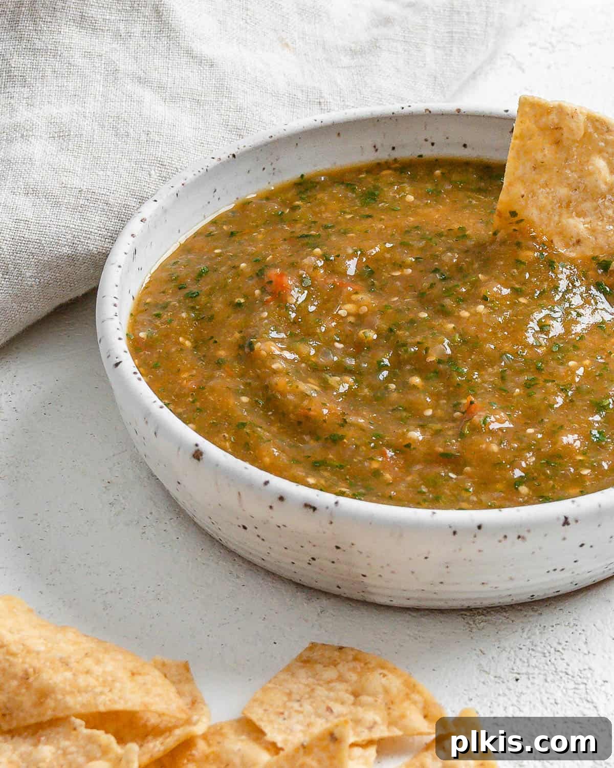 Zesty Tomatillo Green Chili Salsa 13 A close-up shot of the completed Stovetop Tomatillo Salsa in a ceramic bowl, with a single tortilla chip poised for dipping, highlighting its vibrant green color and inviting texture.
