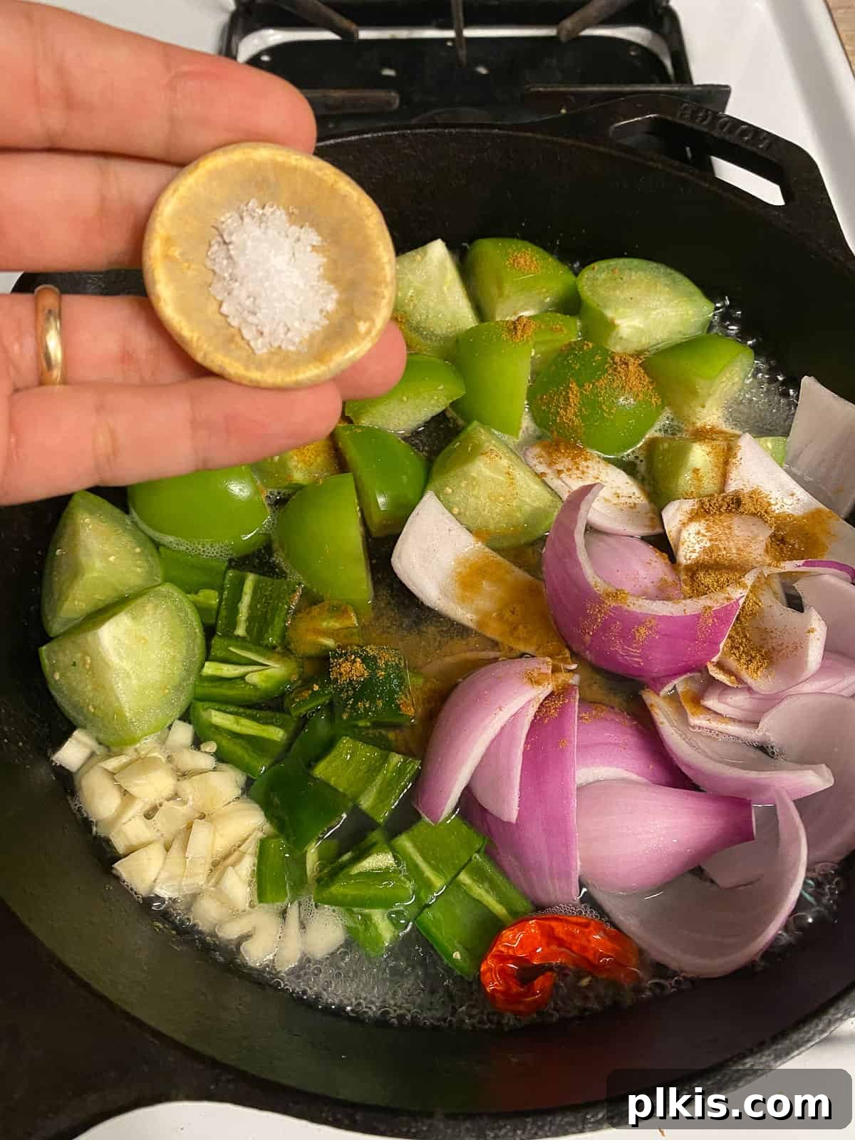 Zesty Tomatillo Green Chili Salsa 7 Sprinkling salt over the vegetables in the saucepan, preparing them for cooking.