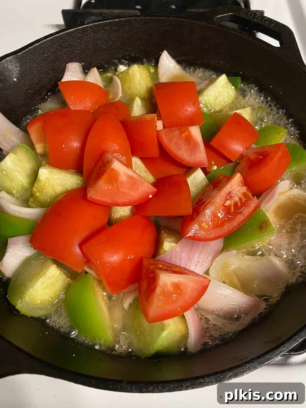 Zesty Tomatillo Green Chili Salsa 8 Adding whole Roma tomatoes to the pan of other chopped vegetables, ready to be cooked down for salsa.