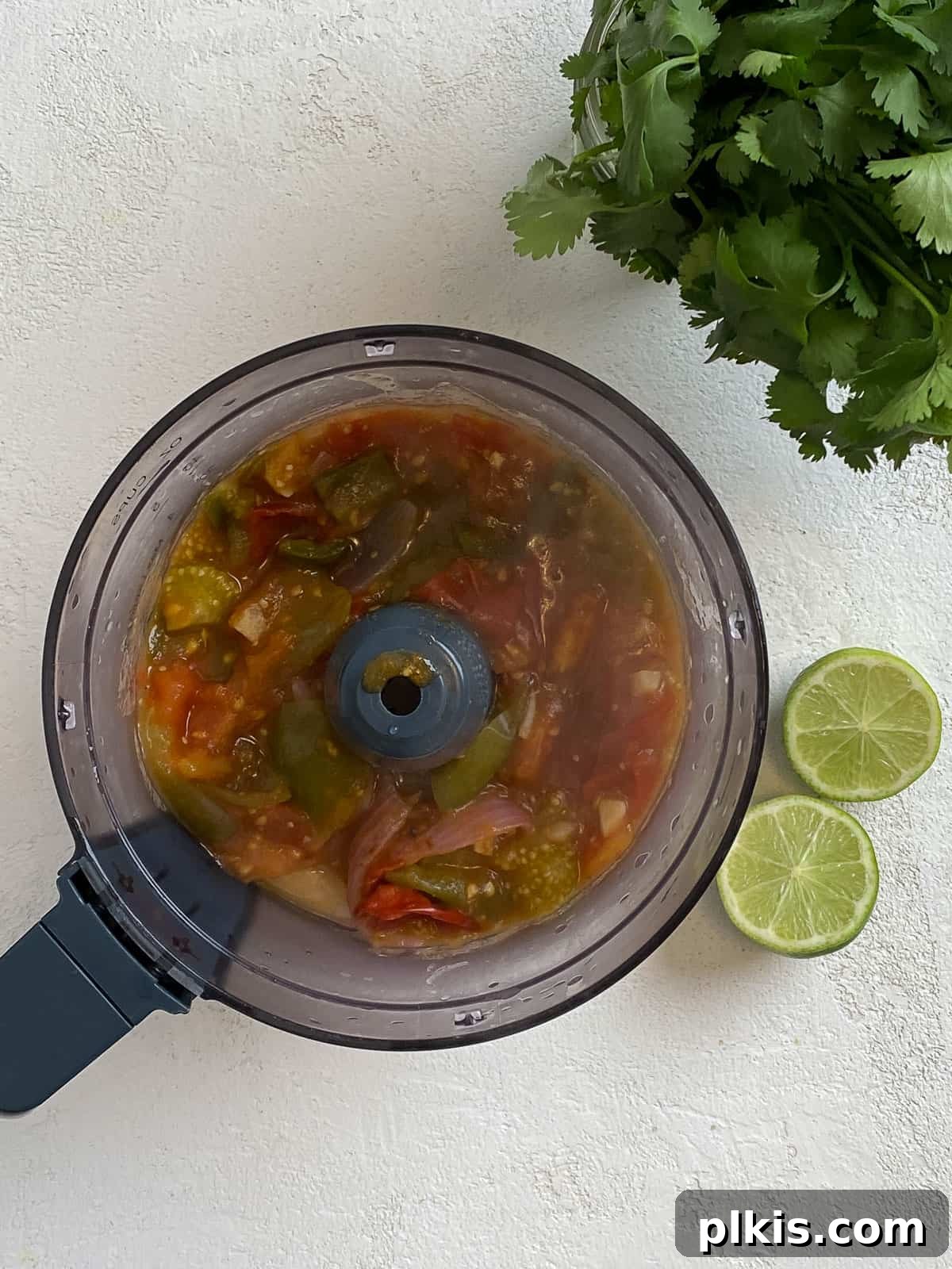 Zesty Tomatillo Green Chili Salsa 10 Cooked vegetables for salsa transferred to a food processor, with fresh cilantro and lime on the side.