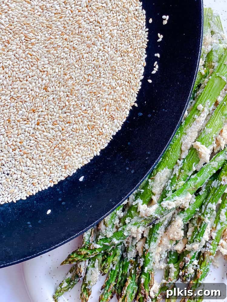Process shot showing sesame seeds being added to asparagus.