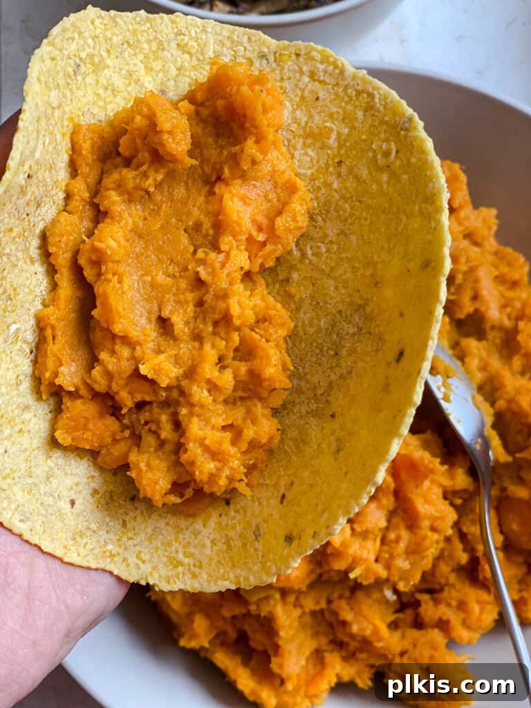 Golden Sweet Potato Rolls 12 Process shot of a spoonful of mashed sweet potato filling being spread onto a warm corn tortilla, ready for rolling.
