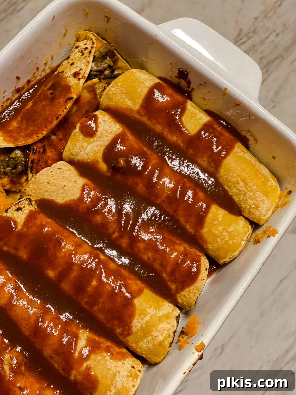 Golden Sweet Potato Rolls 14 Process shot of rolled sweet potato enchiladas arranged in a baking dish, generously covered with rich red enchilada sauce, ready for the oven.