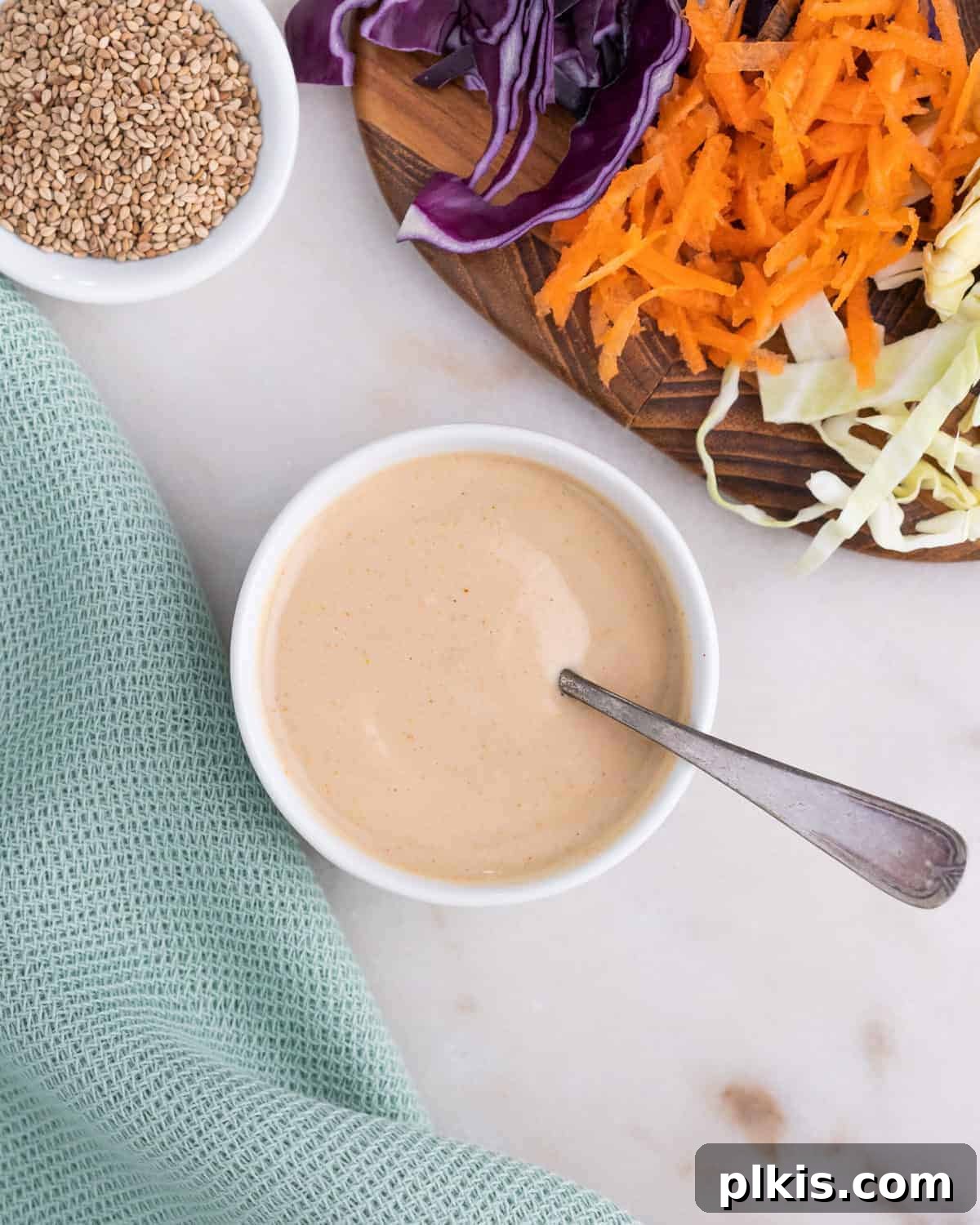 Punchy Coleslaw Dressing 2 completed slaw dressing in a white bowl with a utensil in it along with veggies in the background