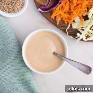 completed slaw dressing in a white bowl with a utensil in it along with veggies in the background