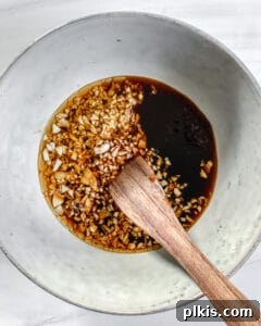 Sweet and Spicy Tofu Stir-Fry 4 Process shot of mixing minced garlic and tamari sauce in a white bowl with a wooden spoon.
