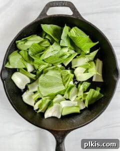 Sweet and Spicy Tofu Stir-Fry 5 Process shot of adding greens (bok choy) to a black pan with water, against a white background.