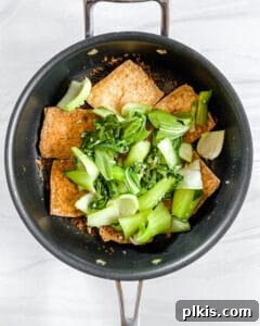 Process shot of adding wilted bok choy to the Spicy and Sweet Tofu in a skillet.