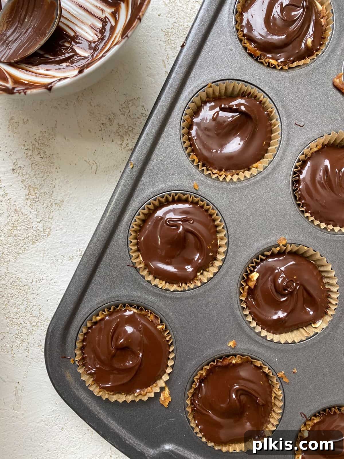 Chilled Peanut Butter Perfection 7 A process shot showing the remaining melted vegan chocolate being carefully poured over the peanut butter and oat bases in the muffin tin, creating a smooth, glossy topping.