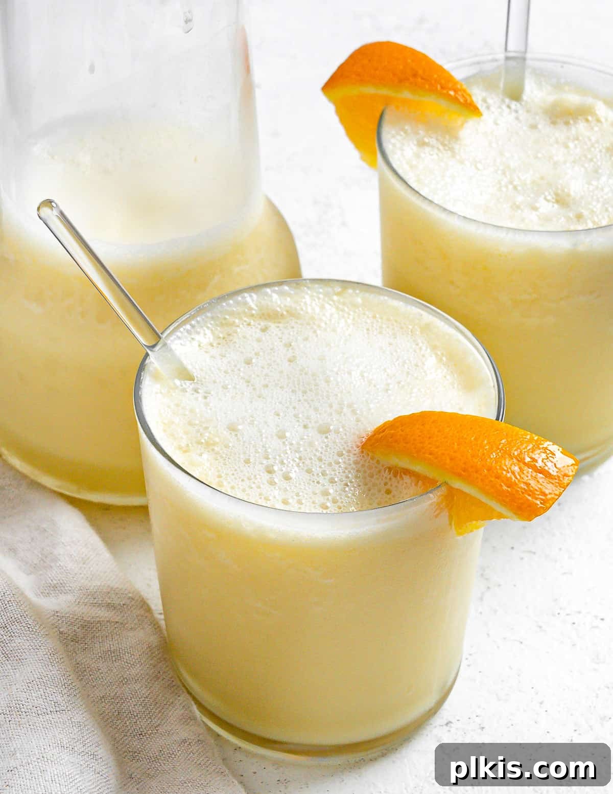 Creamy Orange Dream Smoothie 2 Two completed Easy Orange Julius Smoothies in glass cups with a pitcher in the background, garnished with orange slices and a straw.