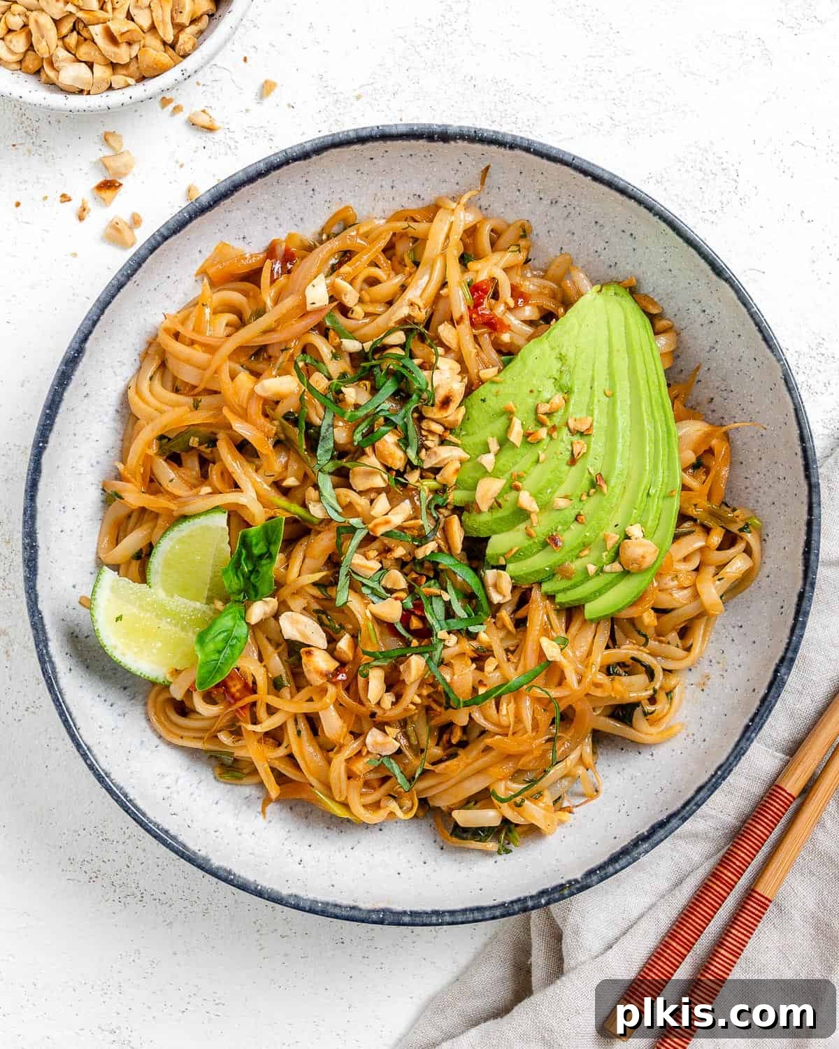 Completed Vegan Vegetable Pad Thai plated against a light background, garnished with peanuts and lime.