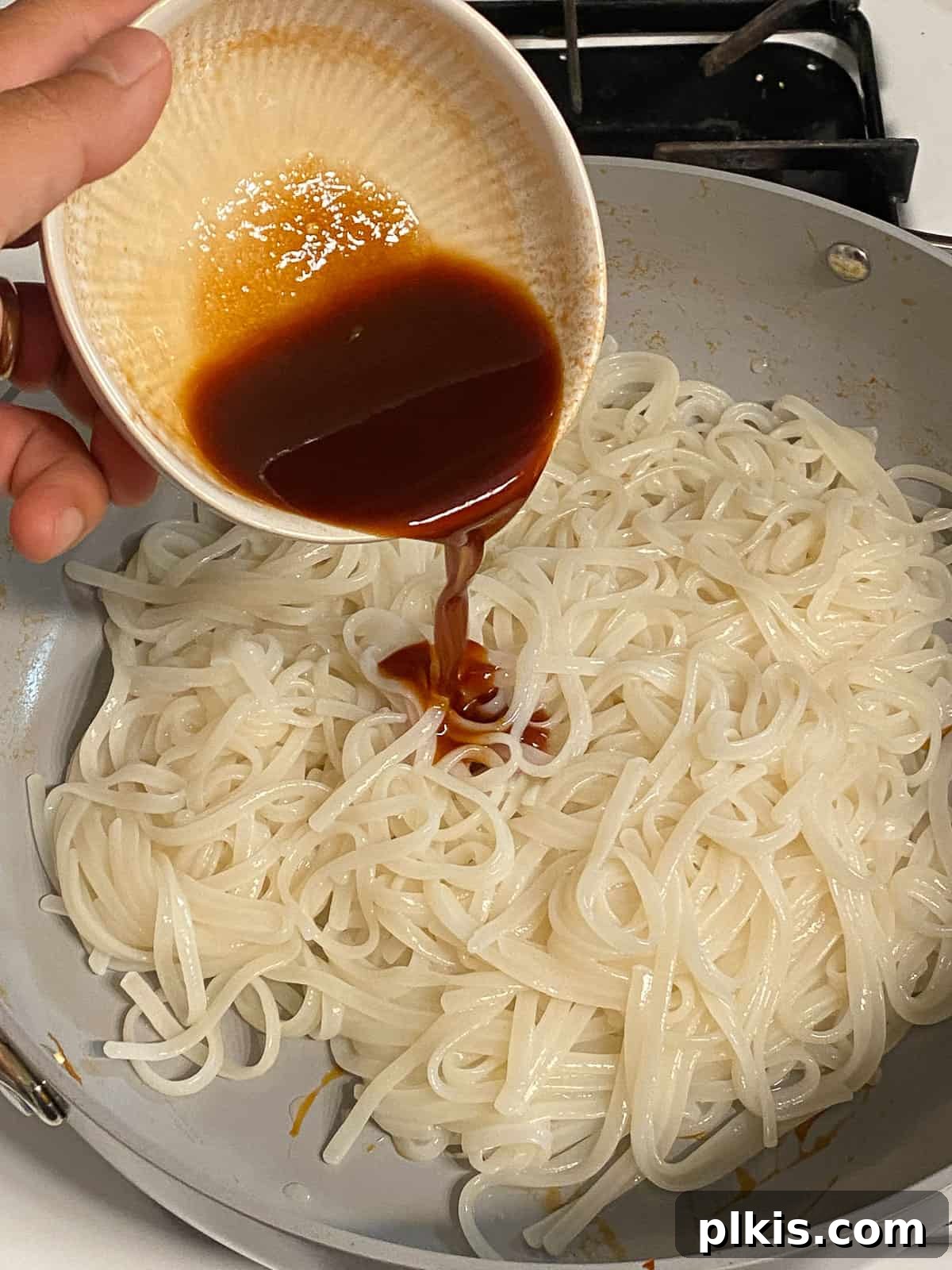 Process of adding additional sauce on top of rice noodles in the pan.