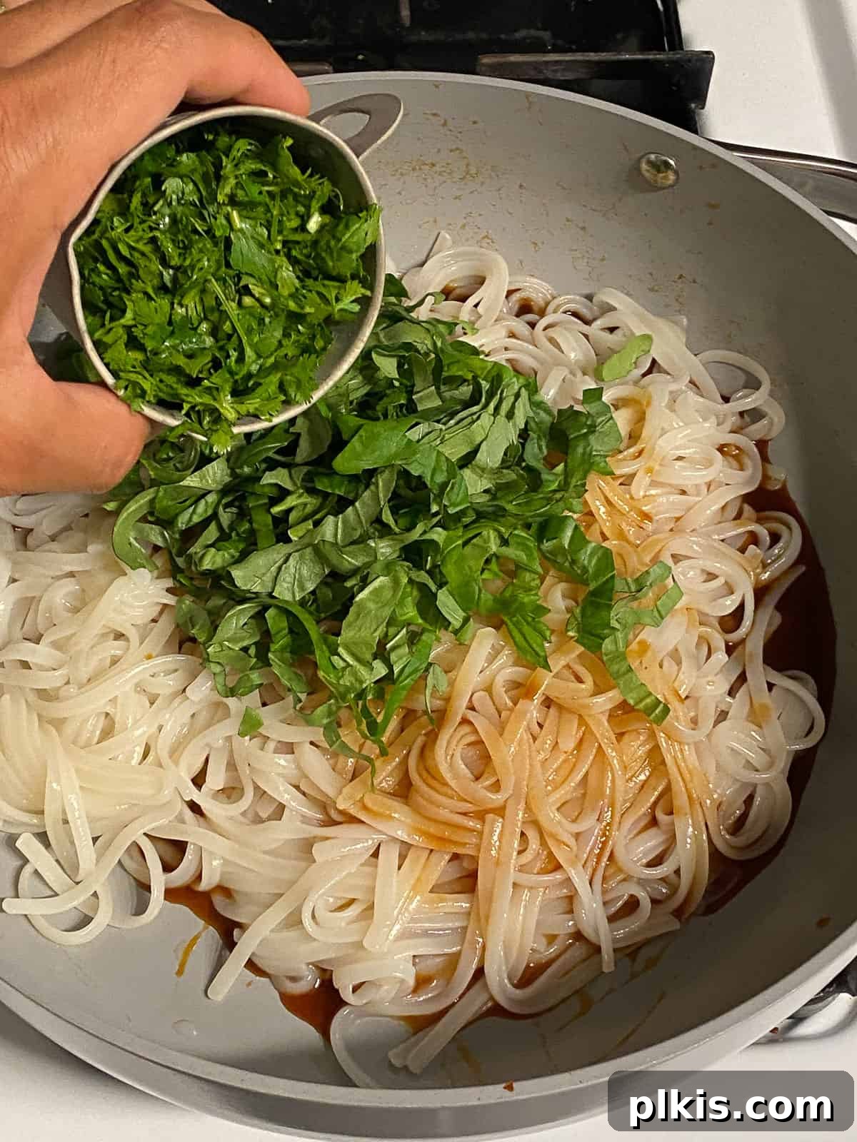 Process of adding fresh cilantro to a pan of noodles.