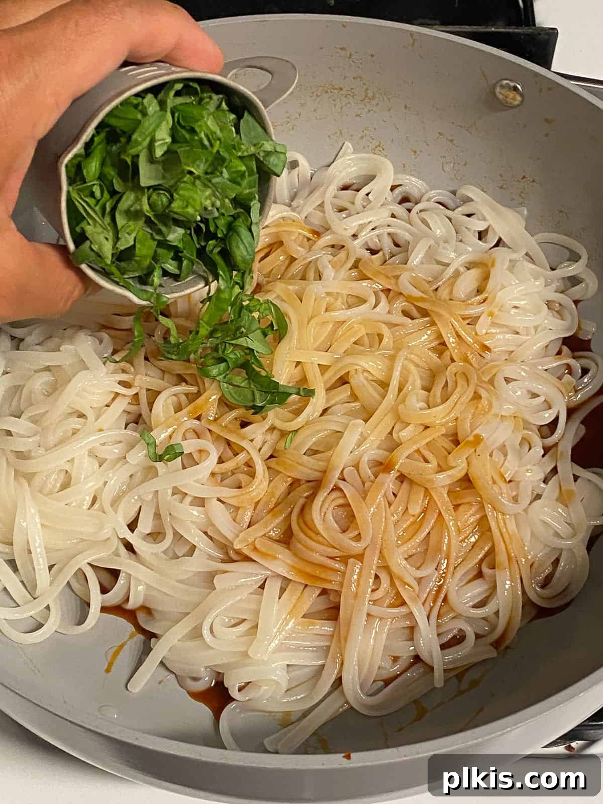 Process of adding fresh basil to a pan of noodles.