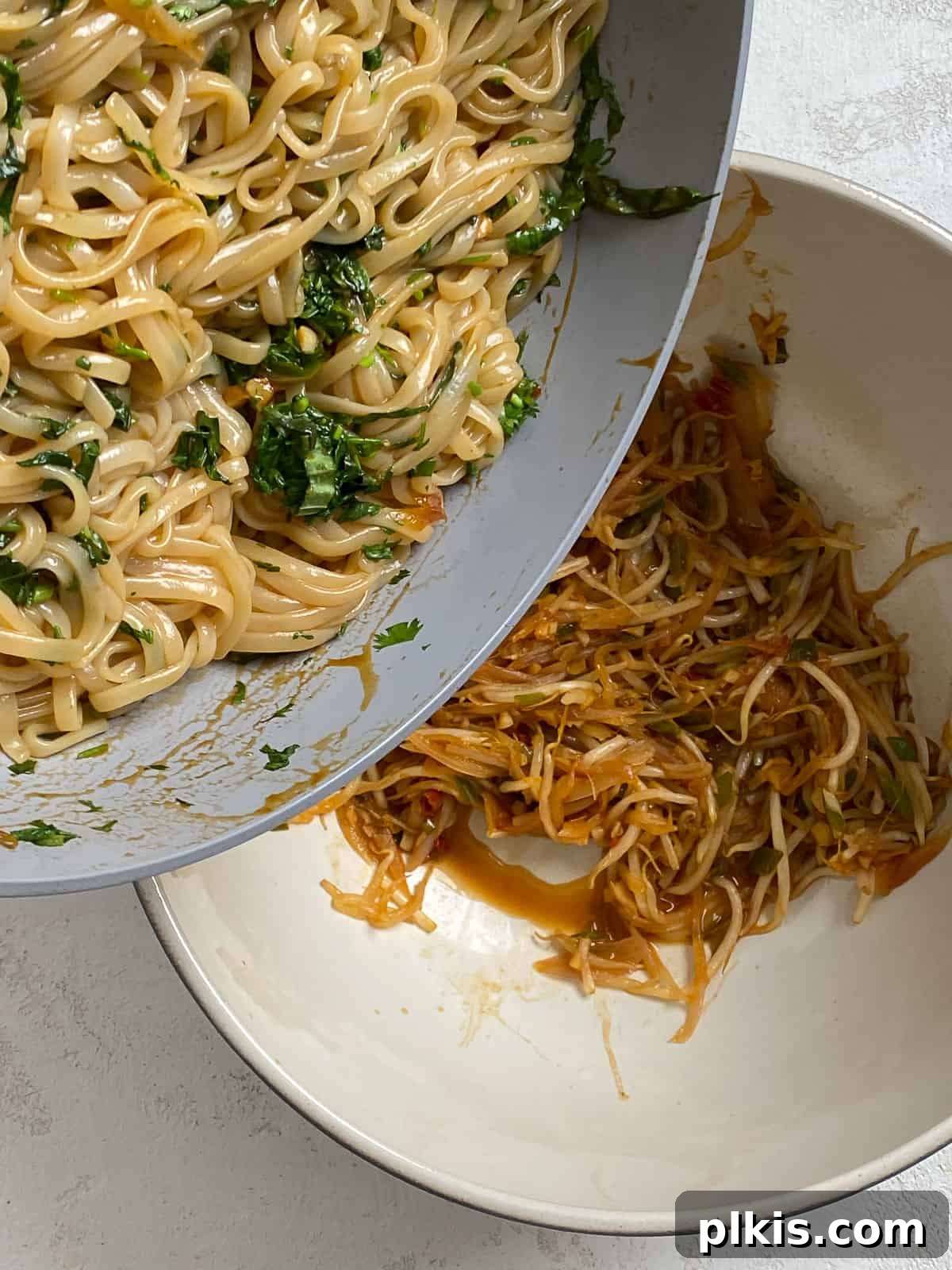 Process of adding cooked rice noodles to a pan of veggies.