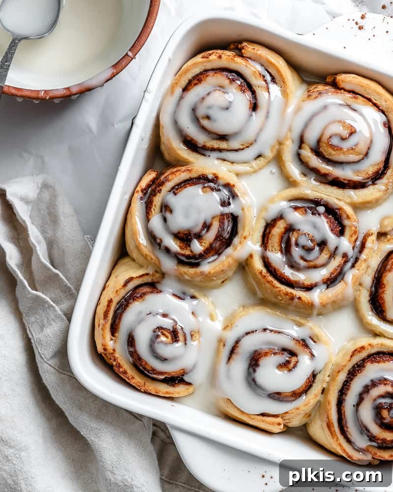 Heavenly Vegan Cinnamon Rolls 2 Perfectly baked vegan cinnamon rolls in a white baking pan, generously drizzled with vanilla icing.