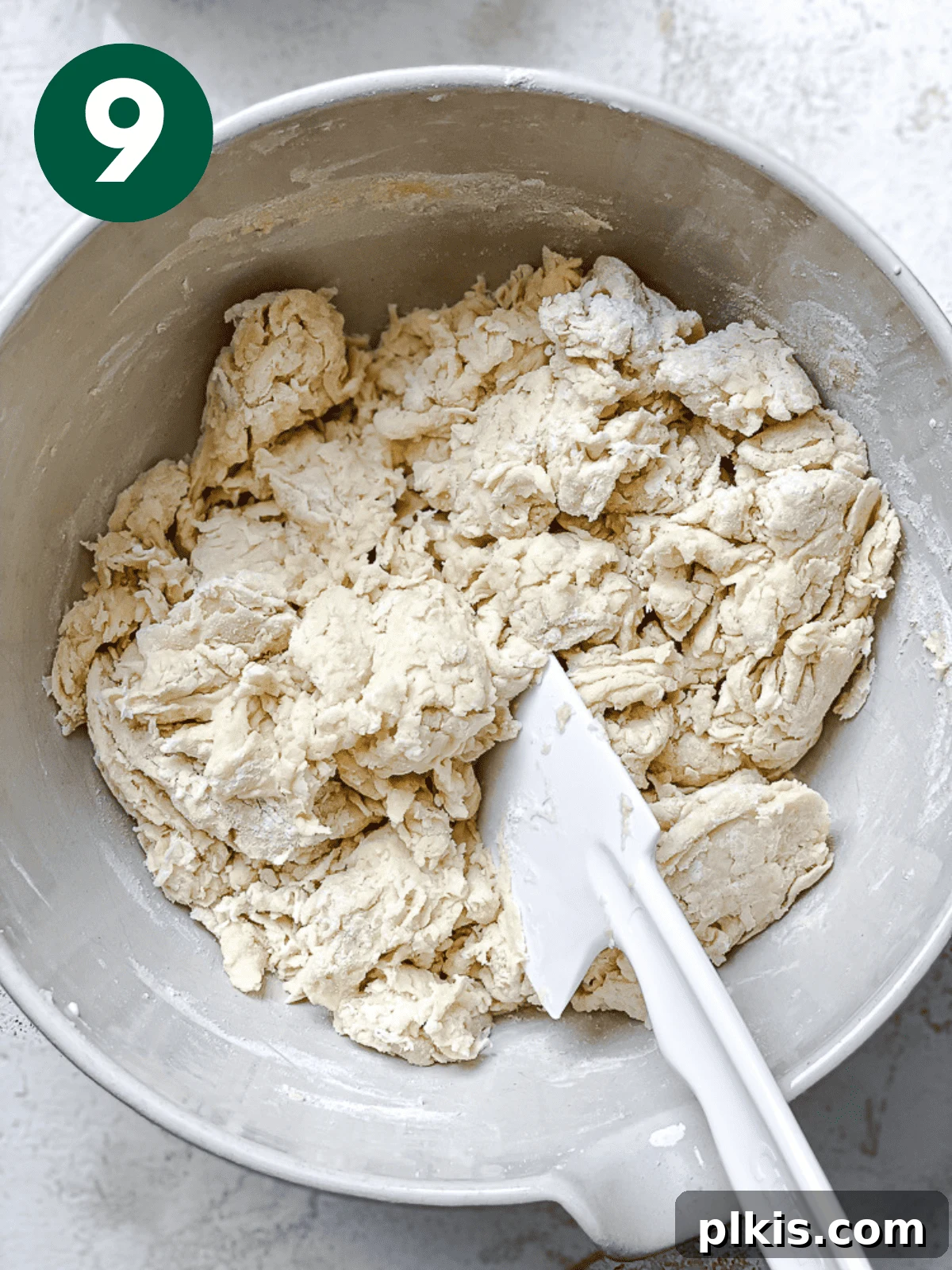 Heavenly Vegan Cinnamon Rolls 12 Using a white spatula to mix the vegan cinnamon roll dough in a large white bowl, showing its initial flaky texture.