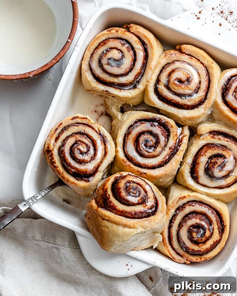Heavenly Vegan Cinnamon Rolls 29 Using a metal spoon to carefully lift a baked vegan cinnamon roll out of a white baking pan.
