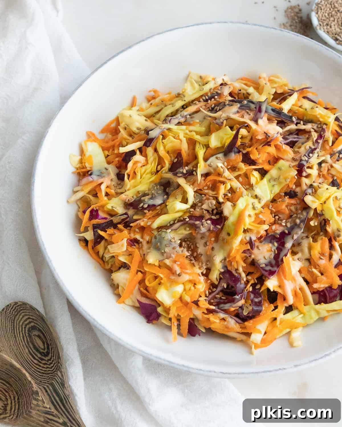 Plant Powered Coleslaw 2 A vibrant bowl of completed vegan coleslaw, featuring colorful shredded cabbage and carrots, garnished with toasted sesame seeds, set against a clean white surface.
