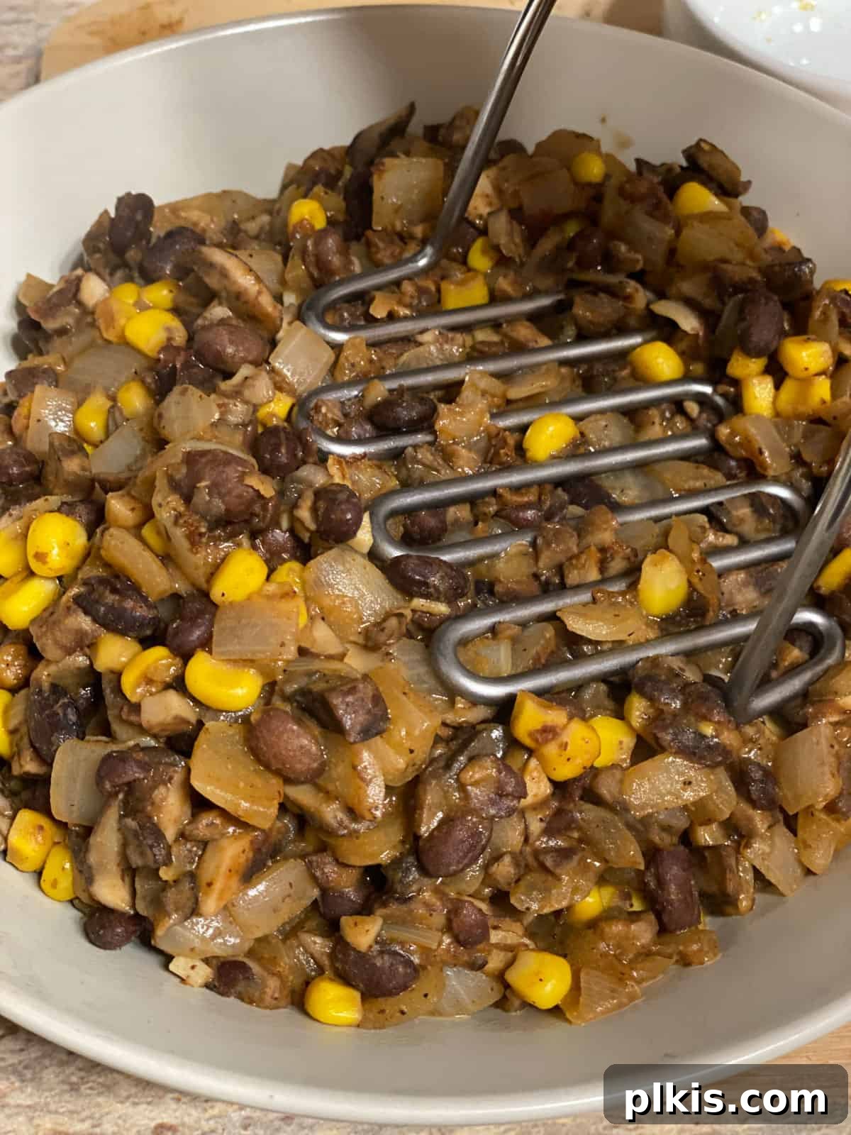 Double the Deliciousness: Vegan Black Bean Tacos 8 process shot of mashing ingredients in a bowl with potato masher