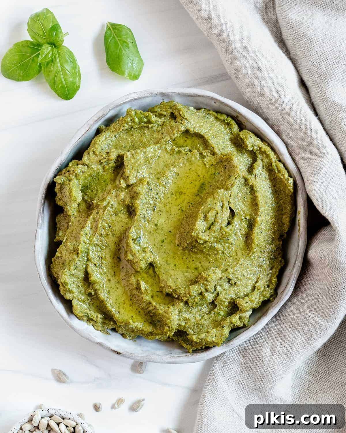 Nut-Free Vegan Basil Pesto with Sunflower Seeds 2 A bowl of vibrant green sunflower seed pesto, garnished with fresh basil leaves, showcasing its creamy texture against a bright background.
