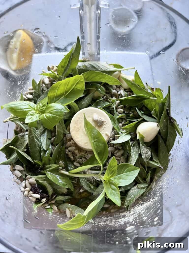 Nut-Free Vegan Basil Pesto with Sunflower Seeds 4 A food processor being filled with ingredients for Sunflower Seed Pesto, including fresh basil, sunflower seeds, and olive oil, poised for blending.