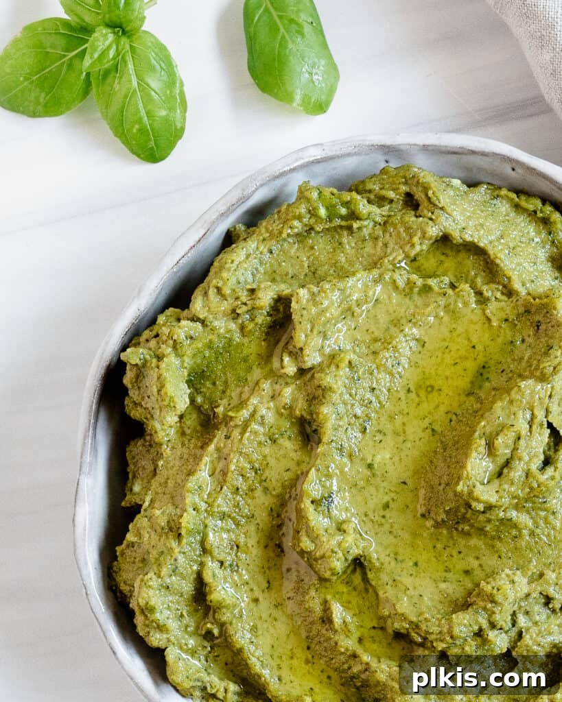 Nut-Free Vegan Basil Pesto with Sunflower Seeds 5 A white bowl filled with creamy, green sunflower seed pesto, ready to be served, against a clean, white background.