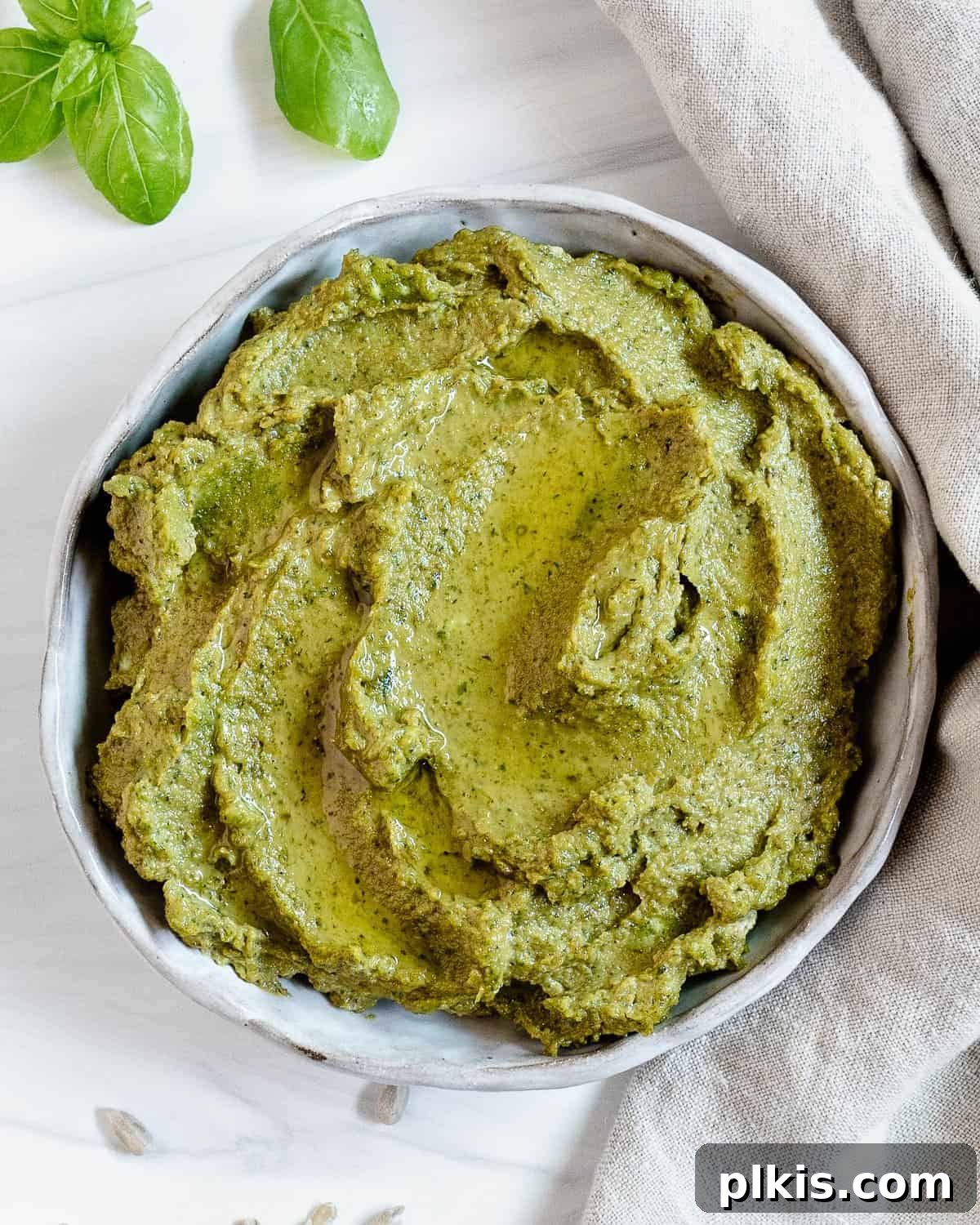 A bowl of vibrant green sunflower seed pesto, ready to be enjoyed, against a bright white background, emphasizing its creamy texture and fresh basil garnish.