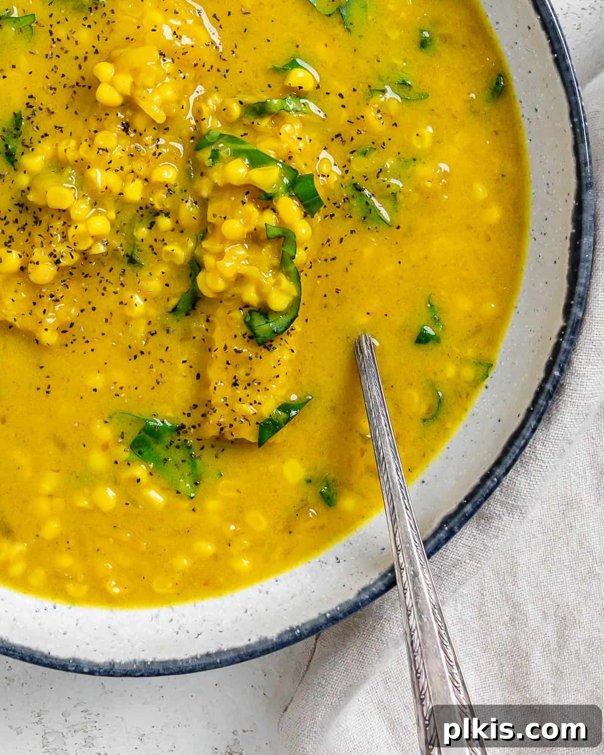 Velvety Vegan Coconut Corn Chowder 16 A close-up shot of creamy vegan corn chowder with coconut milk in a bowl, showcasing its rich texture and fresh basil garnish.