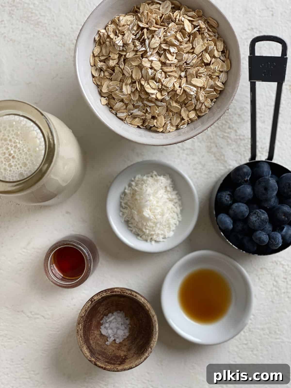 Overnight Blueberry Delight 3 A flat lay photograph showcasing the simple, fresh ingredients required for Blueberry Overnight Oats, including rolled oats, fresh blueberries, plant-based milk, vanilla extract, and a natural sweetener, arranged on a clean white surface.