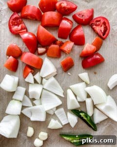 Handcrafted Roasted Red Salsa 4 Roughly chopped vegetables, including tomatoes, onions, and jalapeños, neatly arranged in a single layer on a baking tray, ready for roasting.