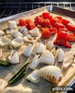 Handcrafted Roasted Red Salsa 5 Close-up view of vegetables roasting in an oven on a baking tray, showing the beginning of browning and charring, indicating they are almost ready.