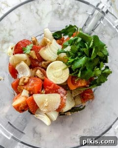 Handcrafted Roasted Red Salsa 7 A food processor bowl filled with roasted vegetables, brown sugar, salt, apple cider vinegar, and fresh cilantro, poised to be blended into homemade salsa.