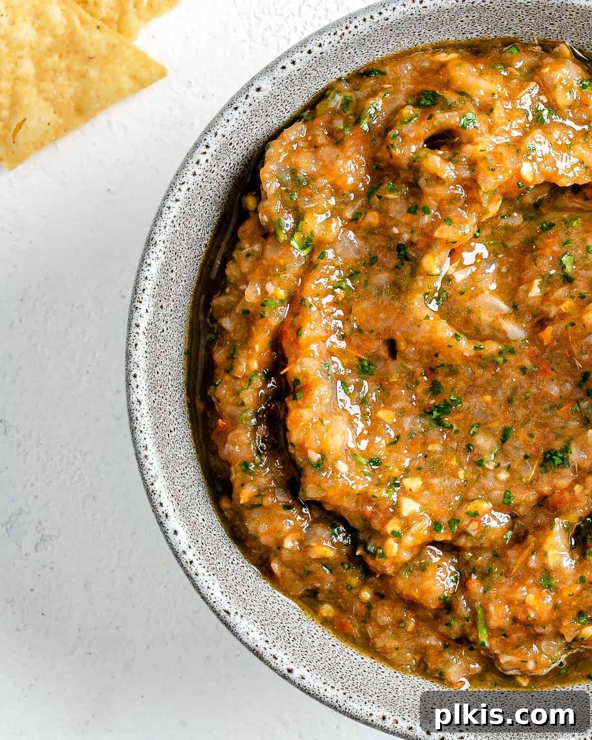 Handcrafted Roasted Red Salsa 8 A pristine white bowl showcasing the finished Homemade Roasted Red Salsa, artfully garnished with fresh cilantro, positioned against a soft white background, with a scattering of crunchy tortilla chips in the background, ready for dipping.