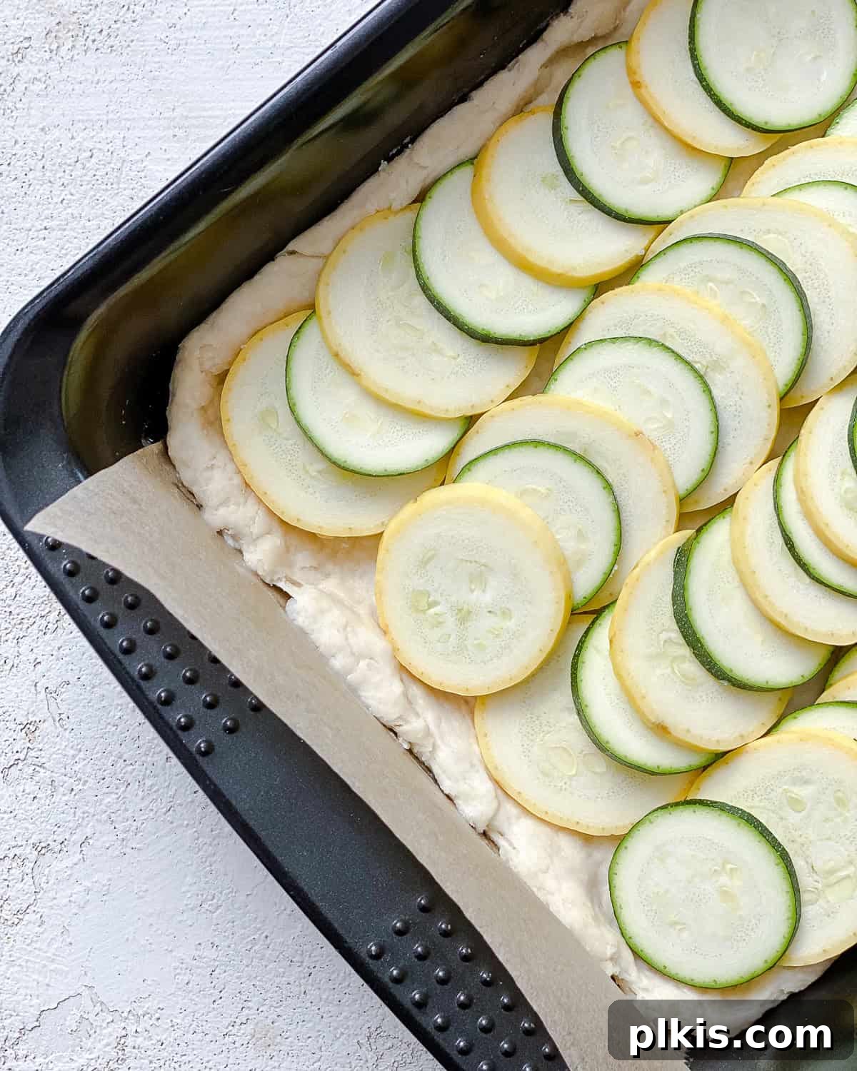 Vibrant Zucchini Tart 9 Artfully arranged slices of zucchini and summer squash layered in neat rows on top of the tart dough in a baking dish.
