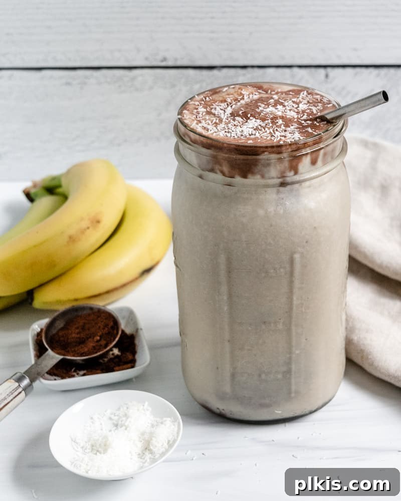 Chocolate Peanut Butter Banana Dream 2 Completed Chocolate Peanut Butter Banana Smoothie in a jar with fresh bananas, peanut butter, and cocoa powder in the background