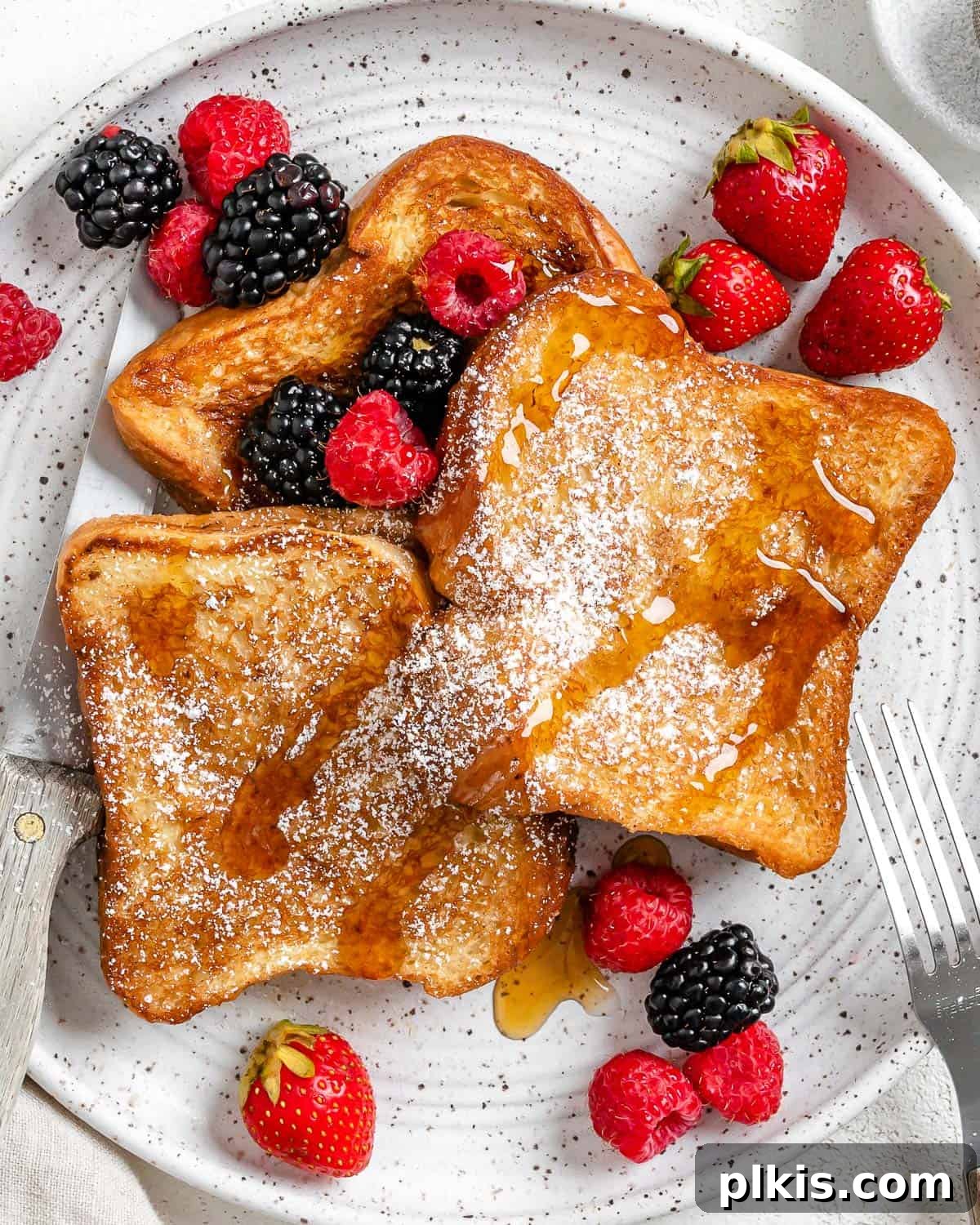 Completed Vegan French Toast plated with fresh mixed berries, sliced banana, and a dusting of powdered sugar on a white plate, ready to be enjoyed.