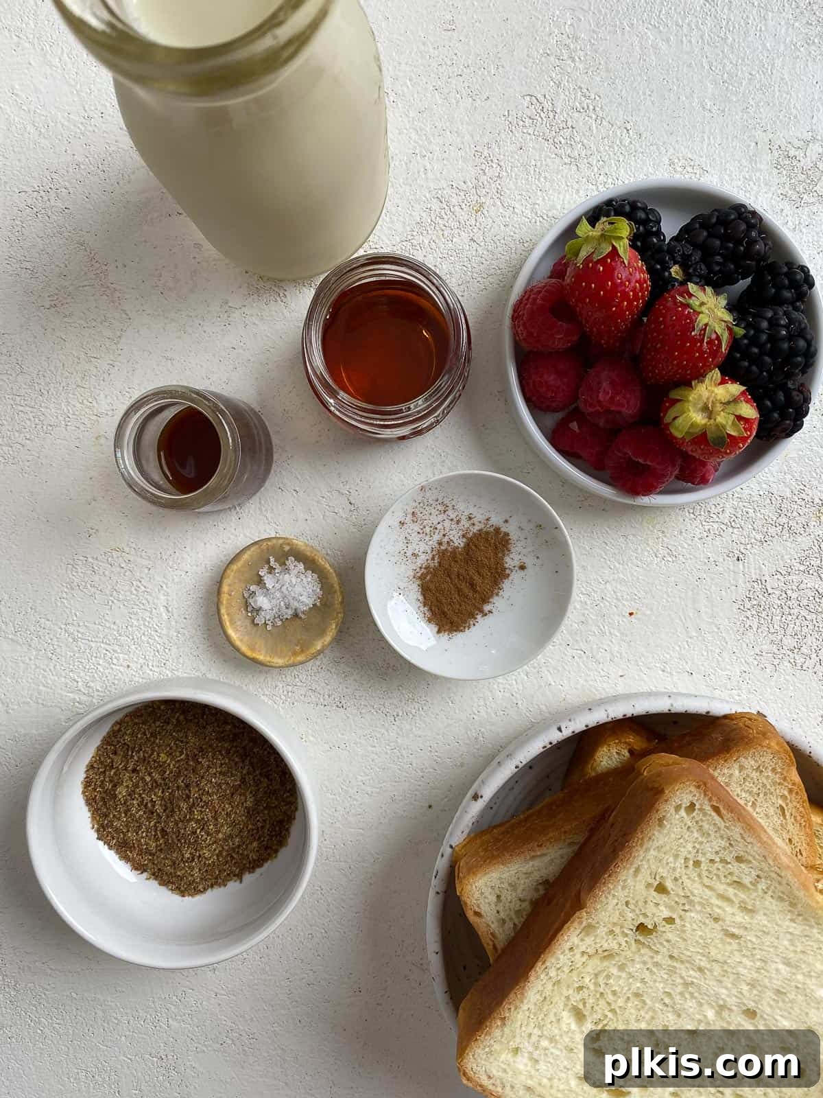 Ingredients for Vegan French Toast laid out on a white background, including ground flaxseed, plant-based milk, agave, vanilla extract, cinnamon, salt, bread slices, and vegan butter.