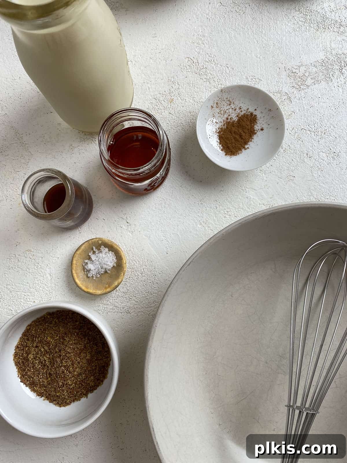 Ingredients for Vegan French Toast measured out on a white background, with a shallow white bowl, whisk, and measuring spoons.