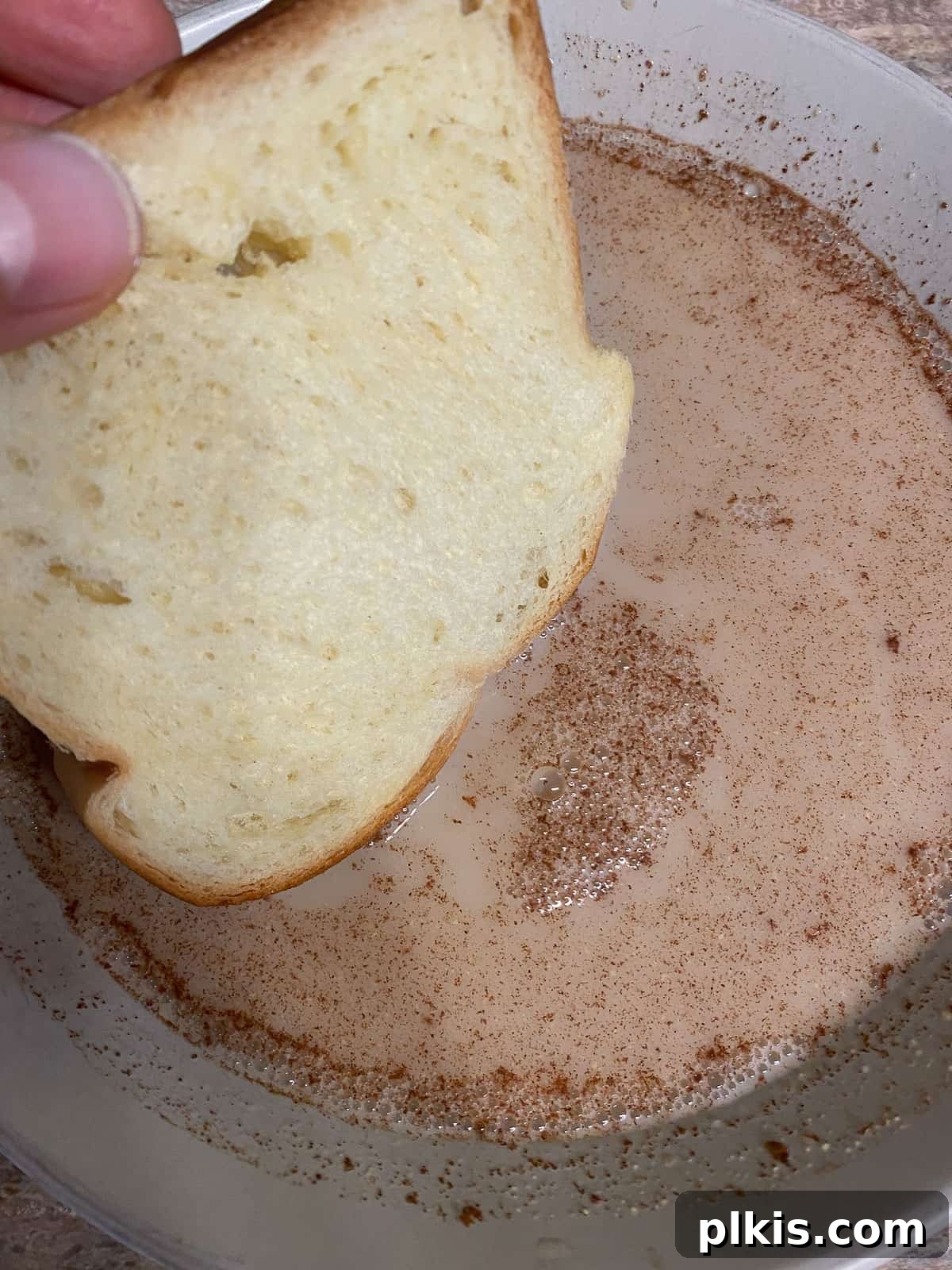 Process shot: A slice of bread being carefully dipped into the vegan French toast batter in a shallow bowl.