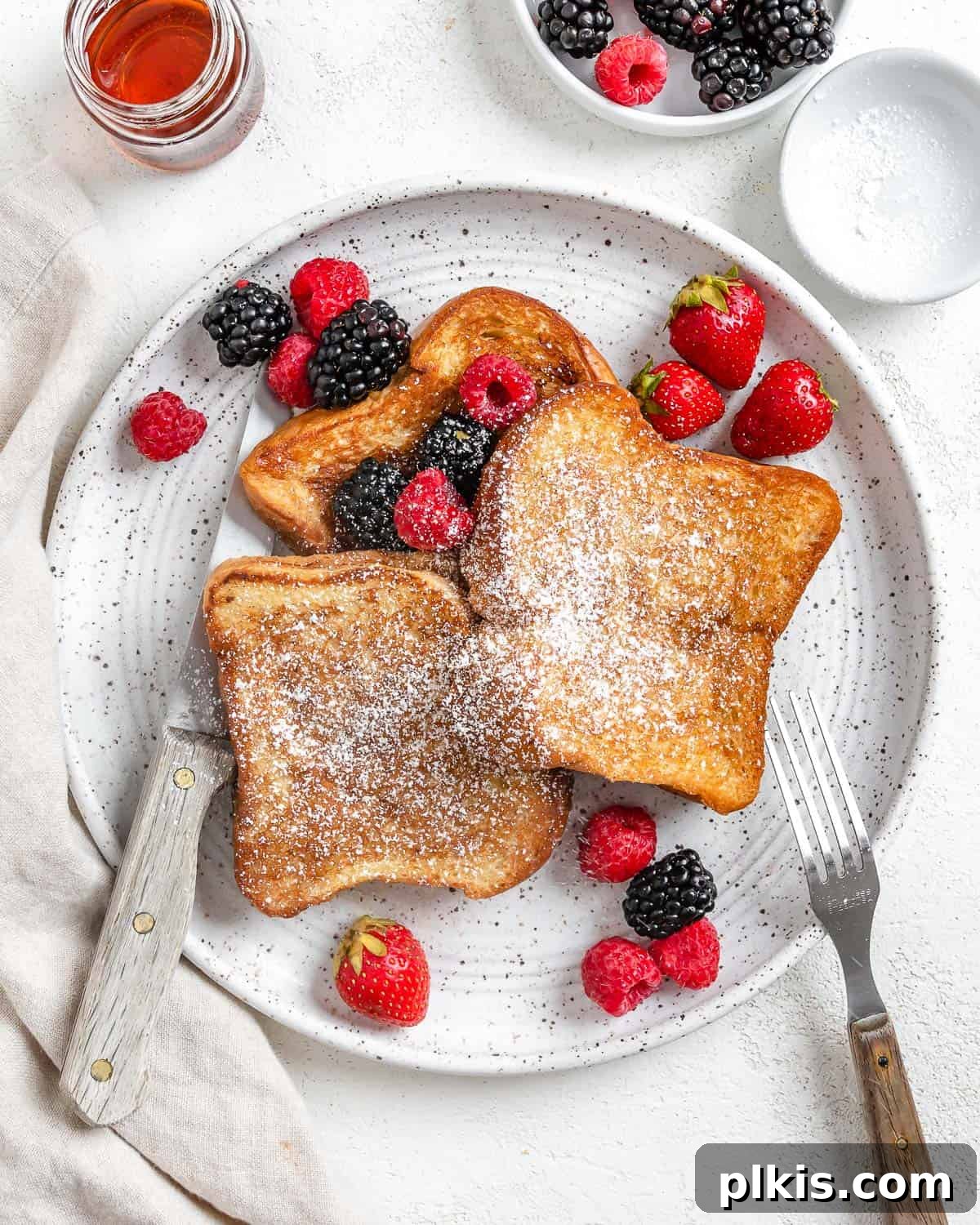 Completed Vegan French Toast plated with fresh fruits, powdered sugar, and a drizzle of maple syrup on a white plate, beautifully garnished.
