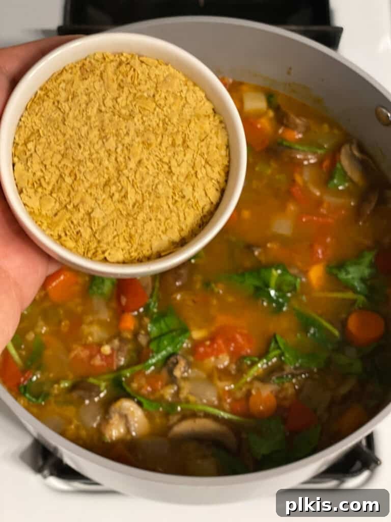 Comforting Red Lentil Stew 13 Nutritional yeast being added to the simmering Hearty Red Lentil Stew for umami flavor.