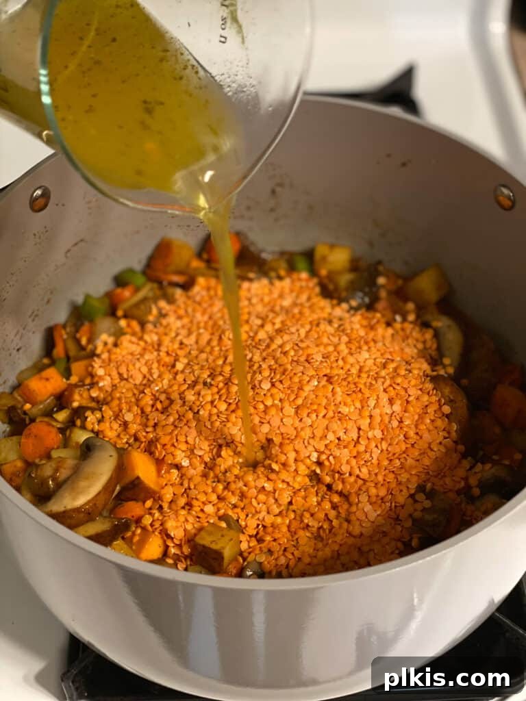 Comforting Red Lentil Stew 10 Vegetable broth being poured into the pot with lentils and vegetables, forming the liquid base of the stew.