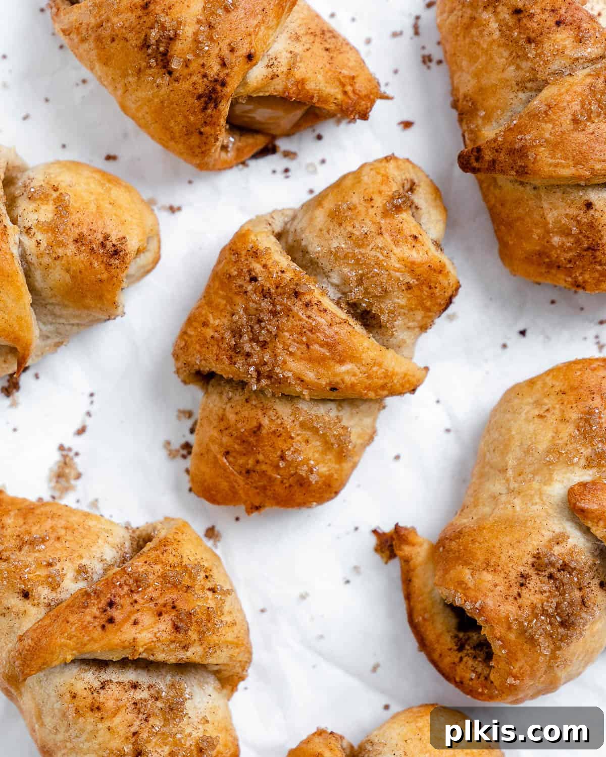 Golden Apple Cinnamon Crescents 2 Golden brown vegan apple crescent rolls sprinkled with sugar on a white surface, ready to be enjoyed.