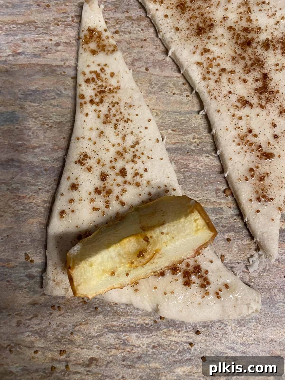 Golden Apple Cinnamon Crescents 11 The process of placing a baked apple slice and rolling it into a crescent roll triangle.